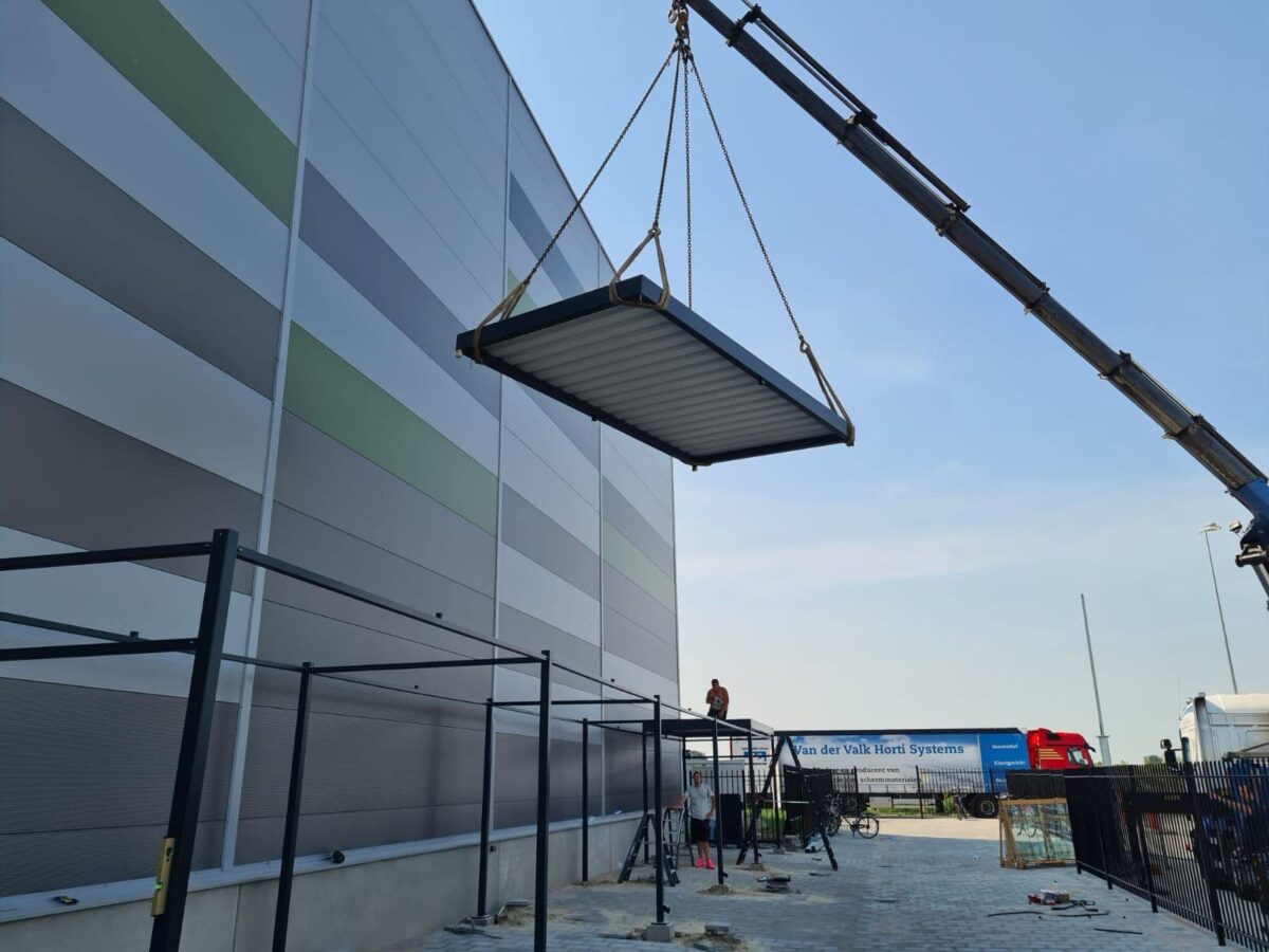 Maatwerk fietsoverkapping Manheim voor gemeente Roosdaal 1 Montage van fietsoverkapping Mannheim 20 meter waarbij het dak met een kraan op de constructie wordt geplaatst in Roosendaal