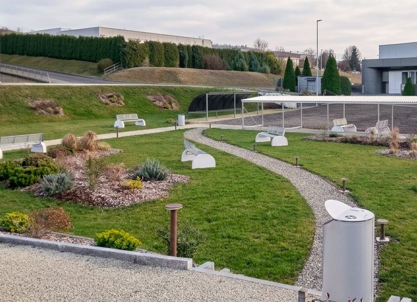 Parkbank Tauri Concrete 9 Parkbanken model Tauri Concrete met betonnen zijsteunen geplaatst in een parkachtige omgeving.