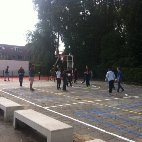 Beton banken 15 U-banken geplaatst in Amsterdam bij een door ons sportief ingericht schoolplein. Pannakooi met basketbal op de achtergrond en 2 losse basketbalpalen en sportbelijningen voor diverse sporten.