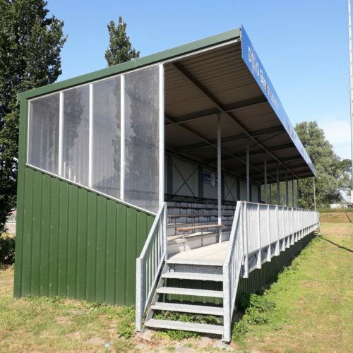Verhoogde overdekte tribune langs sportveld met trapopgang
