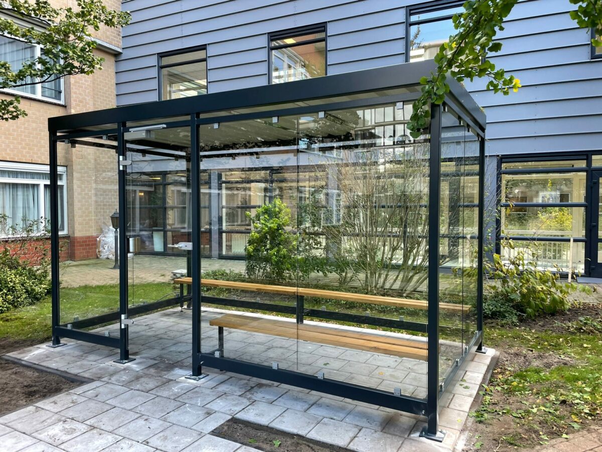 Rookplek buiten inrichten: praktische gids voor bedrijven en organisaties 7 Rookoverkapping Myla 4x2m met zitbanken, deur en groen dak in moderne bedrijfstuin