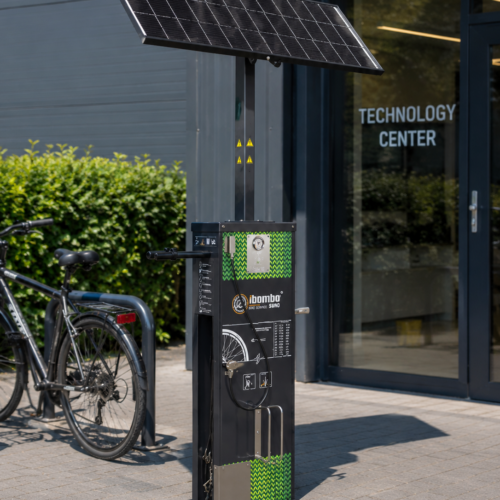 Suno fietsservicestation op zonne-energie met luchtcompressor, gereedschap en USB-oplaadpunt geplaatst bij de entree van een modern bedrijfspand.