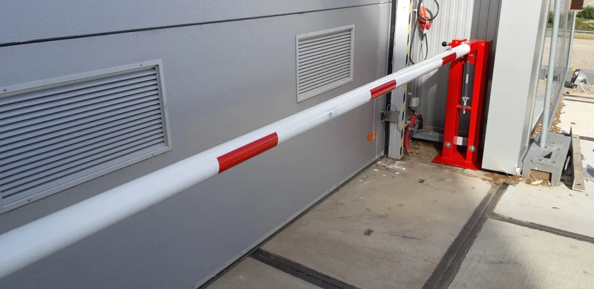 Wat kost een slagboom? Alles over prijzen, uitvoeringen en mogelijkheden 3 Handbediende slagboom met gasveer gemonteerd voor roldeur op fabrieksterrein voor gecontroleerde toegang van voertuigen