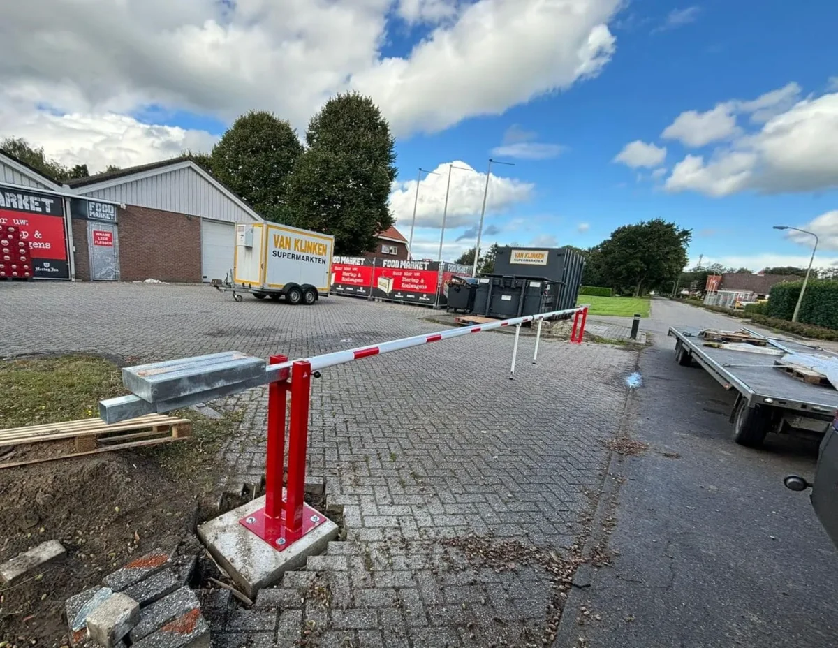 Wat kost een slagboom? Alles over prijzen, uitvoeringen en mogelijkheden 2 Twee handbediende slagbomen met pendelsteun gemonteerd op betonpoeren bij Van Klinken supermarkt in Valthermond