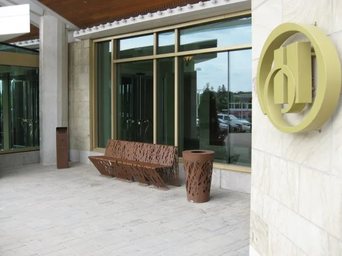 Cortenstalen design parkbank Cross met rugleuning geplaatst tegen een bedrijfsgevel